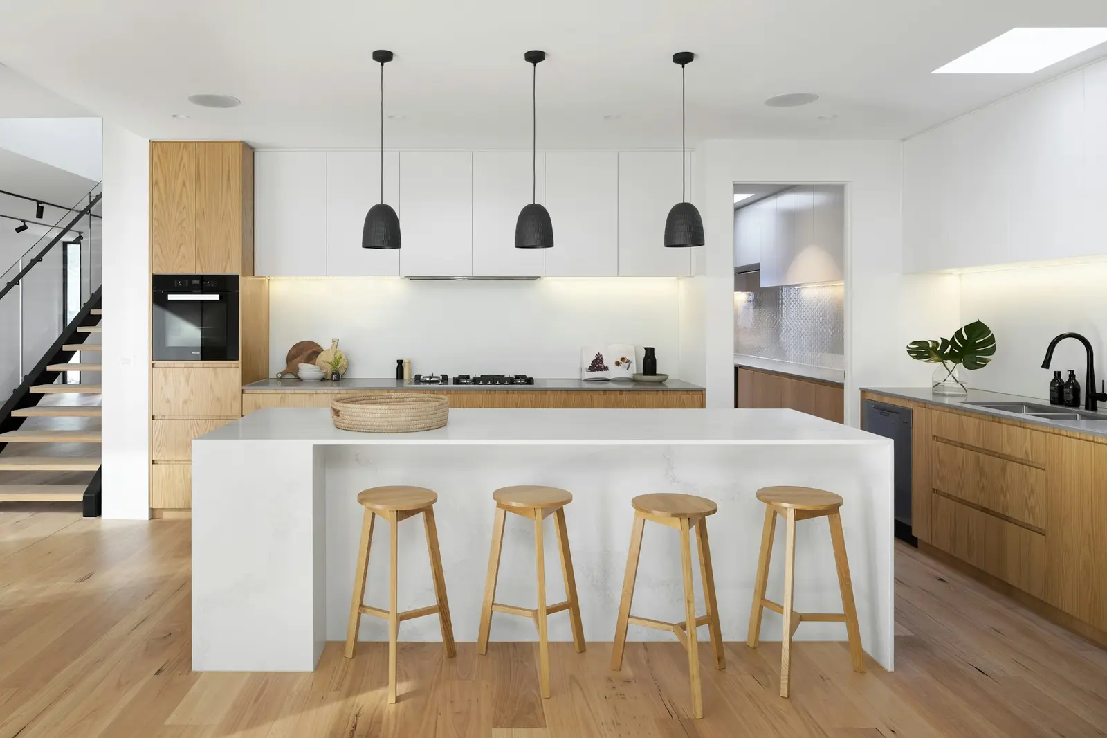 White kitchen with a waterfall island, oak stools and black pendant lights